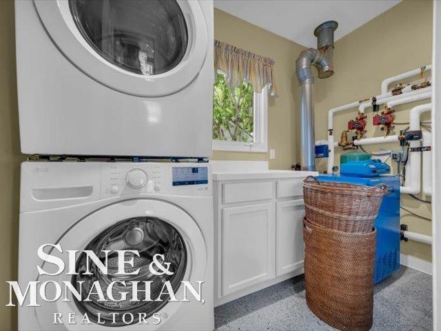 clothes washing area featuring stacked washer / drying machine and cabinet space