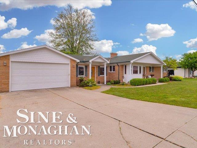 single story home featuring an attached garage, concrete driveway, brick siding, and a front lawn