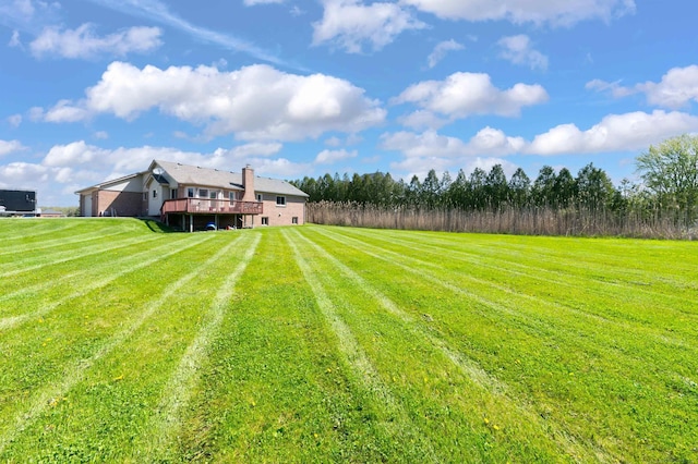 view of green lawn with a wooden deck and a view of rural / pastoral area