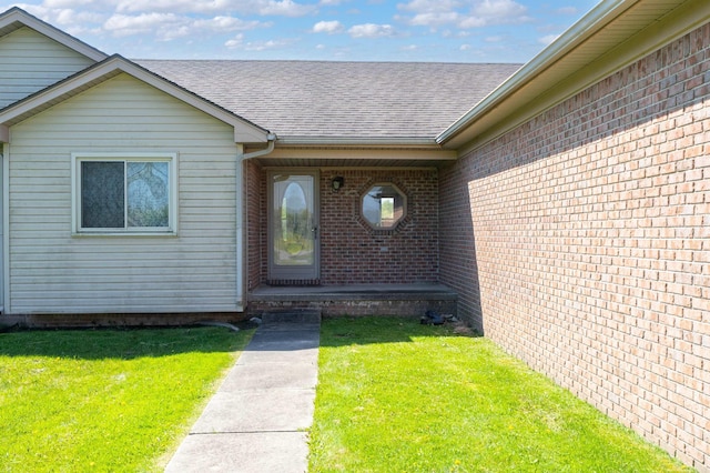 property entrance featuring roof with shingles, a lawn, and brick siding