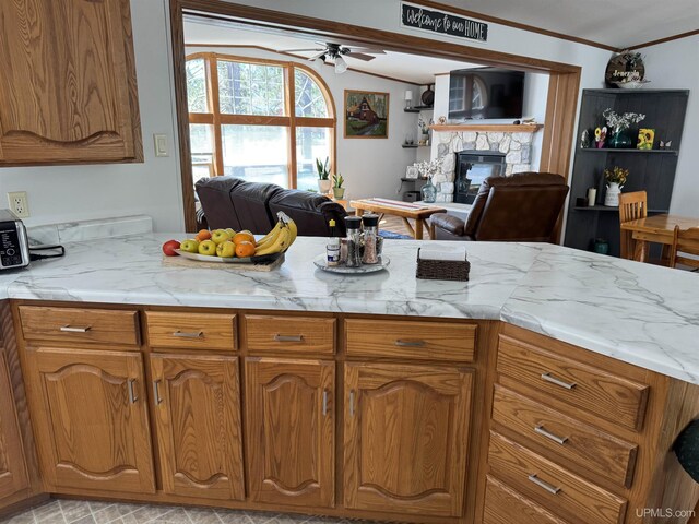 93 E Johnson Lake Rd, Gwinn, MI 49841 - kitchen with open floor plan, a ceiling fan, a stone fireplace, brown cabinets, and ornamental molding
