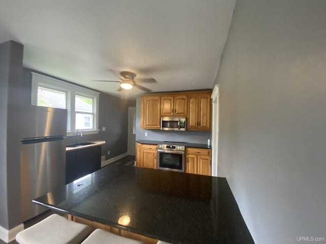 317 Lane Ave, Iron Mountain, MI 49802 - kitchen featuring appliances with stainless steel finishes, a sink, dark countertops, a ceiling fan, and brown cabinetry