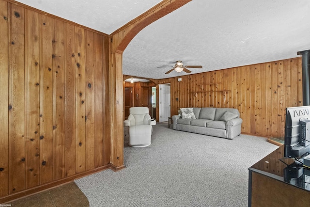 3710 N River Rd, Fort Gratiot, MI 48059 - carpeted living room with arched walkways, a textured ceiling, a ceiling fan, wood walls, and a wood stove
