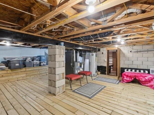 5631 W Spring Knoll Dr, Bay City, MI 48706 - unfinished below grade area featuring gas water heater, wood-type flooring, heating unit, and concrete block wall
