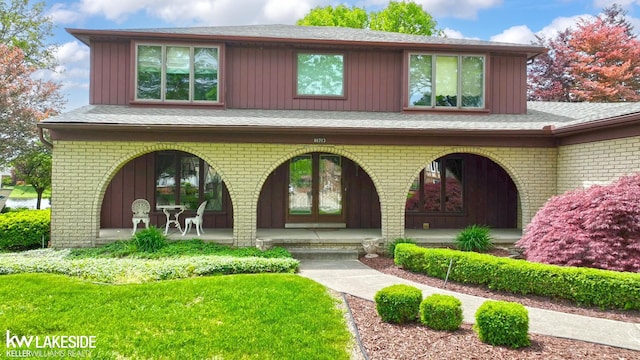 46713 Houghton Dr, Shelby Twp, MI 48315 - view of exterior entry with covered porch, brick siding, board and batten siding, and a shingled roof