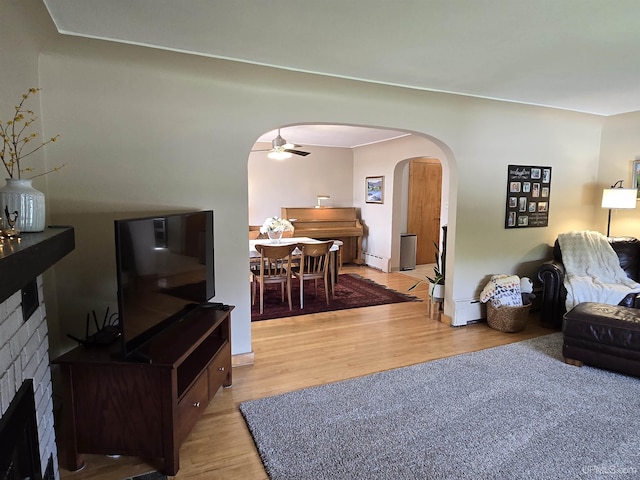 817 W Water St, Hancock, MI 49930 - living area with arched walkways, light wood-style floors, a ceiling fan, a brick fireplace, and a baseboard radiator