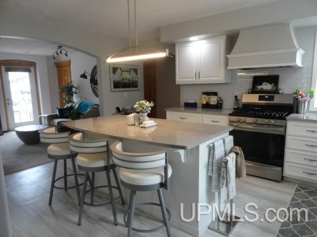 201 E Jewell St, Munising, MI 49862 - kitchen with stainless steel gas range oven, custom range hood, arched walkways, a center island, and white cabinetry