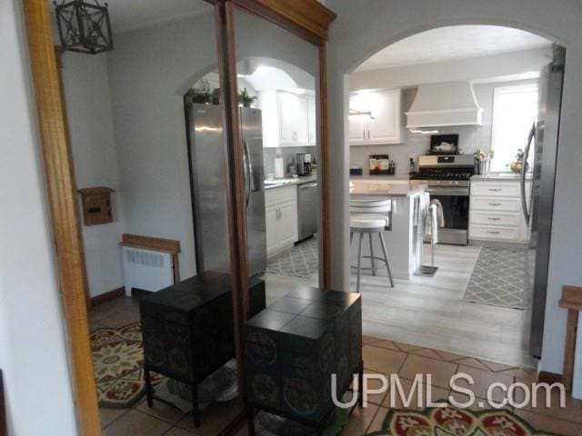 201 E Jewell St, Munising, MI 49862 - kitchen featuring custom range hood, appliances with stainless steel finishes, radiator heating unit, arched walkways, and white cabinets