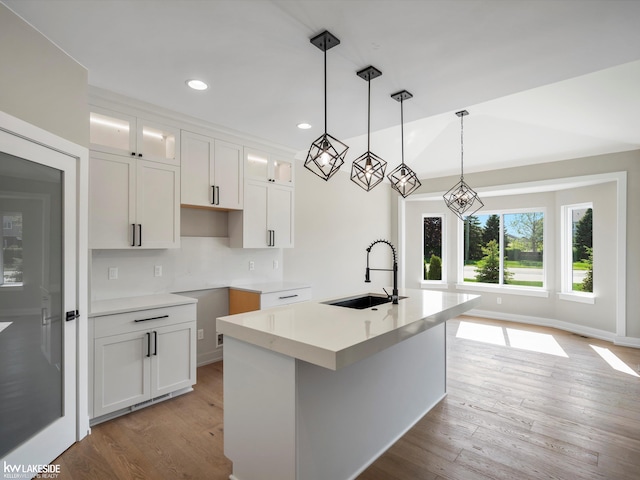 55127 Saint Paul Dr, Macomb Twp, MI 48042 - kitchen with a sink, glass insert cabinets, light wood finished floors, a kitchen island with sink, and white cabinetry