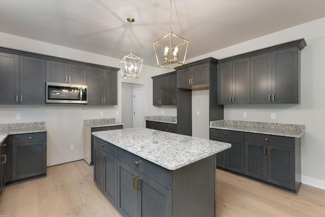 29126 Brooke Meadows Ct, Chesterfield, MI 48047 - kitchen featuring stainless steel microwave, a chandelier, light wood-style flooring, a center island, and decorative light fixtures