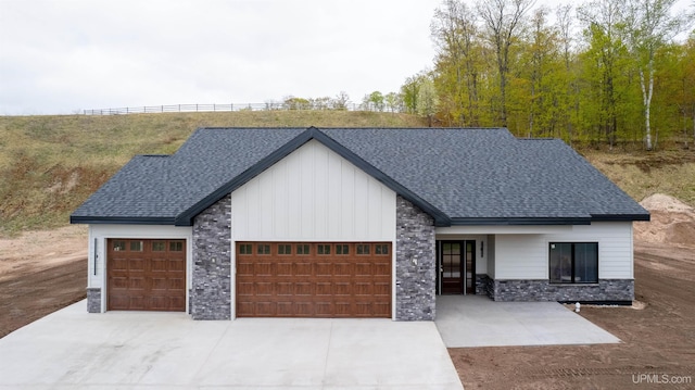 1026 Red Oak Ln, Houghton, MI 49931 - modern farmhouse featuring stone siding, board and batten siding, a garage, concrete driveway, and a shingled roof