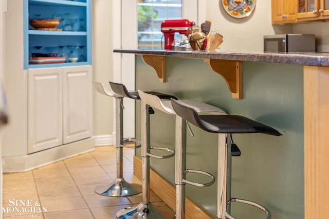 255 Lewiston Rd, Grosse Pointe Farms, MI 48236 - kitchen featuring light tile patterned floors, dark countertops, glass insert cabinets, and a kitchen bar