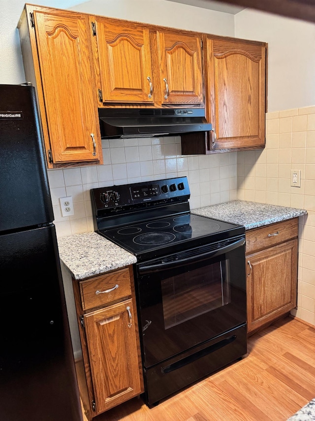 28724 Sutherland Dr, Warren, MI 48088 - kitchen featuring black appliances, under cabinet range hood, light wood-style floors, brown cabinets, and light stone countertops