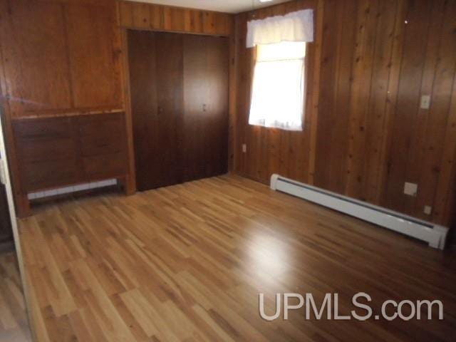 605 W 5th St, Rockland, MI 49960 - unfurnished bedroom featuring a baseboard heating unit, wood finished floors, wood walls, and a closet