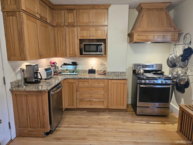 968 Baldwin Ave, Negaunee, MI 49866 - kitchen featuring stainless steel appliances, custom exhaust hood, light wood-style floors, light stone countertops, and brown cabinets