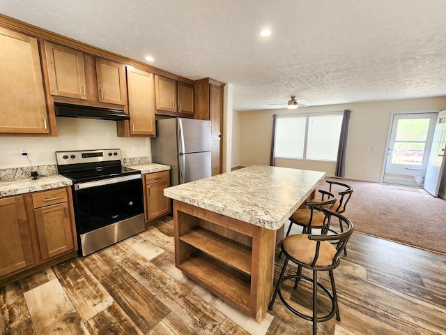 2521 Bonnie Mae Rd, Harrison, MI 48625 - kitchen featuring appliances with stainless steel finishes, under cabinet range hood, a breakfast bar area, wood finished floors, and brown cabinets