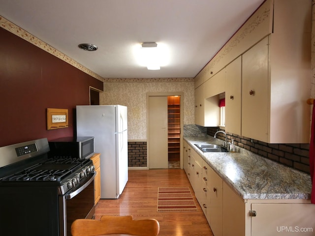 50 Baltic Ave, South Range, MI 49963 - kitchen featuring appliances with stainless steel finishes, a sink, wallpapered walls, light wood-type flooring, and decorative backsplash