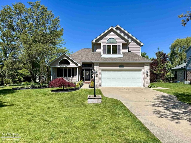1080 Highland Dr, Saint Clair, MI 48079 - traditional home with driveway, an attached garage, a front lawn, brick siding, and roof with shingles