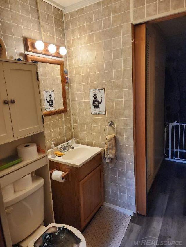 6669 Lakeshore Rd, Lexington, MI 48450 - bathroom with tile walls, toilet, vanity, wood finished floors, and ornamental molding