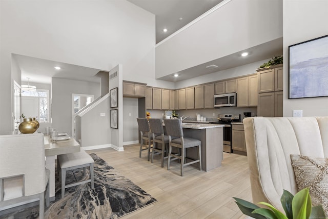 2215 Chase Dr Unit 102, Howell, MI 48855 - kitchen with appliances with stainless steel finishes, a high ceiling, a kitchen bar, baseboards, and light wood-style floors
