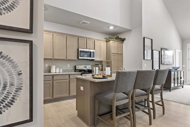 2215 Chase Dr Unit 102, Howell, MI 48855 - kitchen with appliances with stainless steel finishes, a kitchen bar, light wood-style flooring, high vaulted ceiling, and a kitchen island with sink