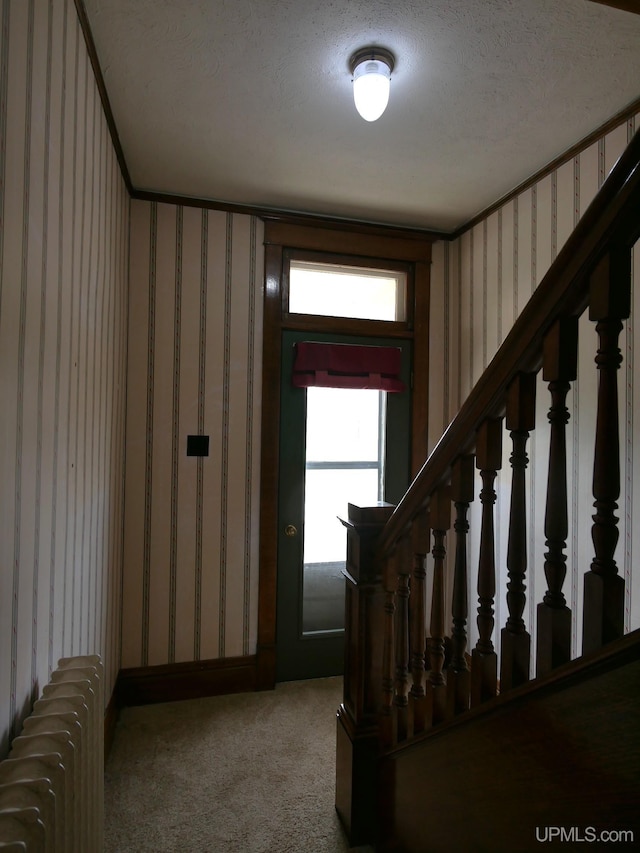909 Quincy St, Hancock, MI 49930 - carpeted foyer entrance with wallpapered walls, radiator heating unit, stairway, and a textured ceiling