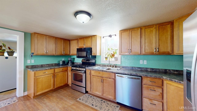 422 Washington St, Ishpeming, MI 49849 - kitchen with stainless steel appliances, a sink, light wood-style floors, dark countertops, and a textured ceiling