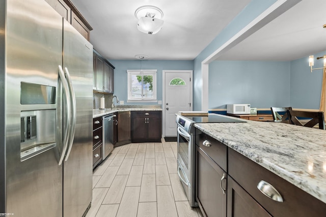 8912 Hubbard St, Livonia, MI 48150 - kitchen featuring appliances with stainless steel finishes, dark brown cabinets, light stone counters, hanging light fixtures, and light wood-type flooring