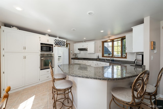 7975 00.25 Rd, Garden, MI 49835 - kitchen with stainless steel appliances, a peninsula, a kitchen breakfast bar, under cabinet range hood, and white cabinets
