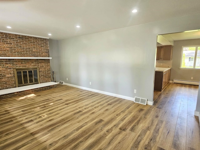 3045 W Birch Dr, Bay City, MI 48706 - unfurnished living room with baseboard heating, wood finished floors, baseboards, recessed lighting, and a brick fireplace