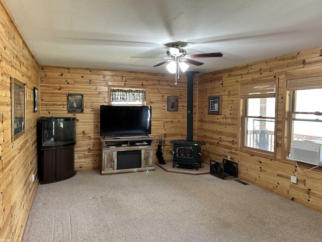 5077 Henry Hwy, Lewiston, MI 49756 - unfurnished living room featuring a wood stove, wooden walls, carpet flooring, a ceiling fan, and cooling unit