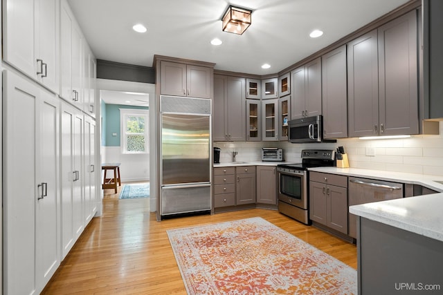 624 E G St, Iron Mountain, MI 49801 - kitchen with appliances with stainless steel finishes, gray cabinetry, decorative backsplash, light wood-type flooring, and glass insert cabinets