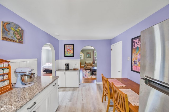 622 Kendon Dr, Lansing, MI 48910 - kitchen featuring freestanding refrigerator, arched walkways, light wood finished floors, light stone counters, and white cabinetry