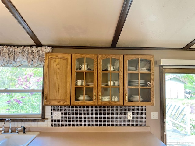 47275 Green Acres Rd, Houghton, MI 49931 - kitchen view of tasteful backsplash, brown cabinetry, glass insert cabinets, a sink, and light countertops