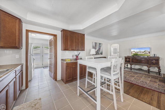 22301 Saint Gertrude St, Saint Clair Shores, MI 48081 - kitchen featuring freestanding refrigerator, light tile patterned floors, decorative backsplash, a raised ceiling, and brown cabinetry