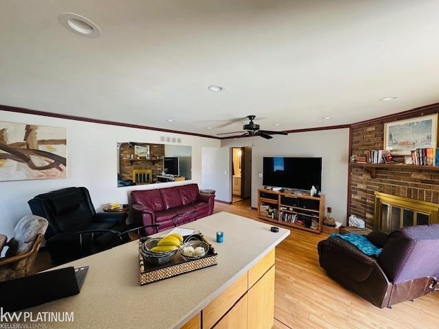 16754 Sarno Dr, Macomb, MI 48044 - living area featuring a brick fireplace, light wood-style floors, ornamental molding, recessed lighting, and a ceiling fan