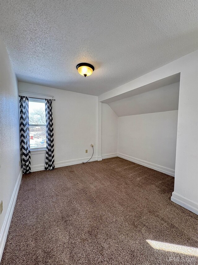 909 Sutherland Ave, Ironwood, MI 49938 - unfurnished room featuring carpet floors, a textured ceiling, baseboards, and vaulted ceiling