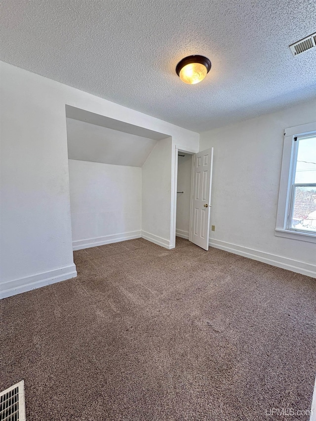 909 Sutherland Ave, Ironwood, MI 49938 - spare room with a textured ceiling, carpet, baseboards, and vaulted ceiling