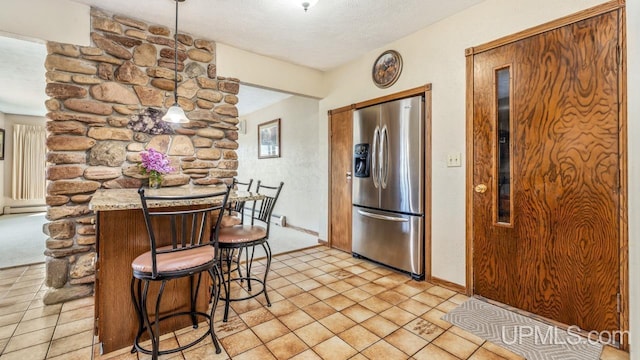 2119 S 21st Ave, Escanaba, MI 49829 - kitchen with stainless steel refrigerator with ice dispenser, a textured ceiling, a kitchen bar, a baseboard heating unit, and baseboards