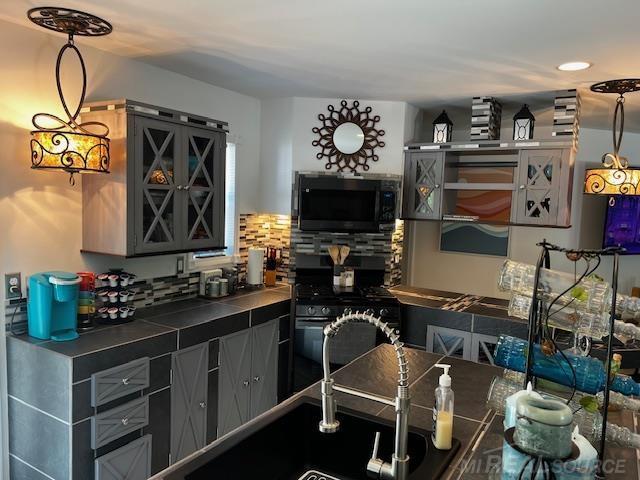 1335 28th St, Manistee, MI 49660 - kitchen with black microwave, tile countertops, decorative backsplash, gray cabinetry, and recessed lighting