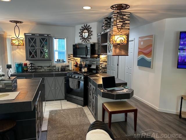 1335 28th St, Manistee, MI 49660 - kitchen featuring black microwave, stainless steel gas range oven, tasteful backsplash, light wood-type flooring, and hanging light fixtures