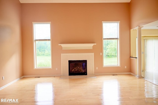 21832 Preserve Ct, Macomb Twp, MI 48042 - unfurnished living room featuring wood finished floors, plenty of natural light, decorative columns, and a fireplace with flush hearth