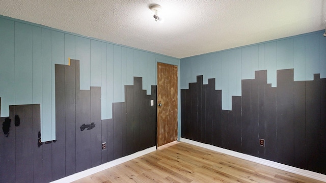13148 Saginaw Rd, Clio, MI 48420 - unfurnished room featuring light wood-style flooring, wooden walls, and a textured ceiling