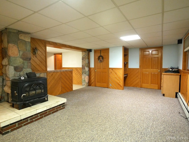 1120 Dextrom Rd, Calumet, MI 49913 - unfurnished living room featuring a wood stove, wood walls, a baseboard radiator, carpet flooring, and a paneled ceiling