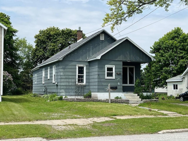 228 Schoolcraft Ave, Manistique, MI 49854 - bungalow-style house featuring board and batten siding, a chimney, and a front yard