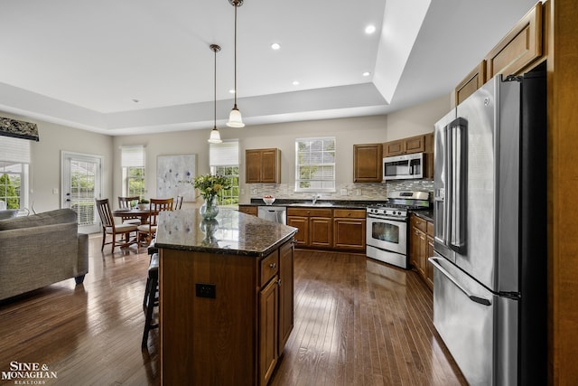 32 River Ln, Grosse Pointe Woods, MI 48236 - kitchen with appliances with stainless steel finishes, a raised ceiling, a kitchen breakfast bar, backsplash, and dark wood-type flooring