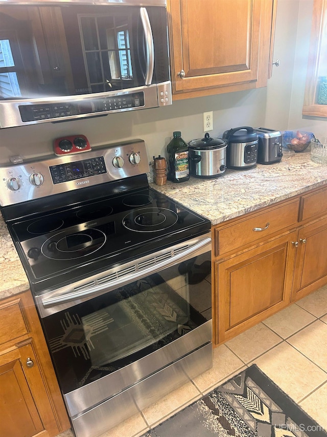 790 N Horseshoe Lake Dr, Gwinn, MI 49841 - kitchen featuring stainless steel appliances, brown cabinetry, light stone countertops, and light tile patterned floors