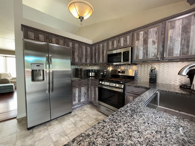 51767 Huntley Ave, New Baltimore, MI 48047 - kitchen featuring stainless steel appliances, dark brown cabinets, decorative backsplash, dark stone counters, and vaulted ceiling