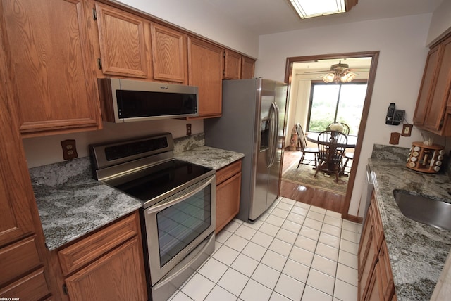 131 Cherryl Ln Unit 4, Algonac, MI 48001 - kitchen featuring stainless steel appliances, light tile patterned floors, brown cabinets, a chandelier, and light stone counters