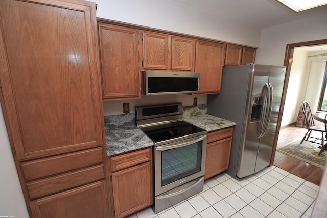 131 Cherryl Ln Unit 4, Algonac, MI 48001 - kitchen featuring stainless steel appliances, brown cabinetry, light tile patterned floors, and stone countertops